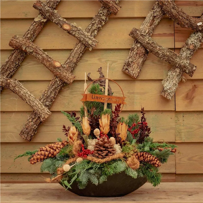 Allerheiligengesteck in dunkler Schale mit Zapfen, Trockenblumen und Holzschild